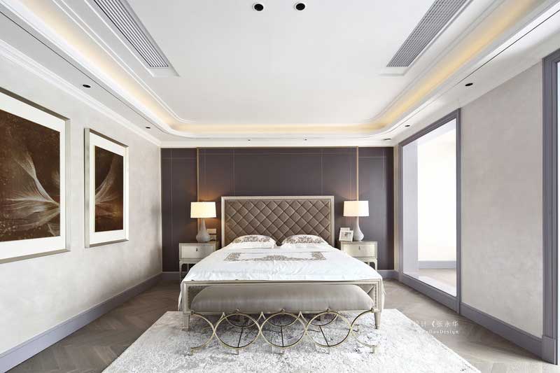 三樓是整個主臥空間，擁有內(nèi)門廳、主臥室、衣帽間、衛(wèi)生間等。主臥背景選用深灰色的硬包裝飾，加上金屬線條的點(diǎn)綴，讓整個背景不顯呆板。主臥陽臺同樣打通與臥室形成一體，局部空間做了地臺，讓整個空間既寬敞又有層次。