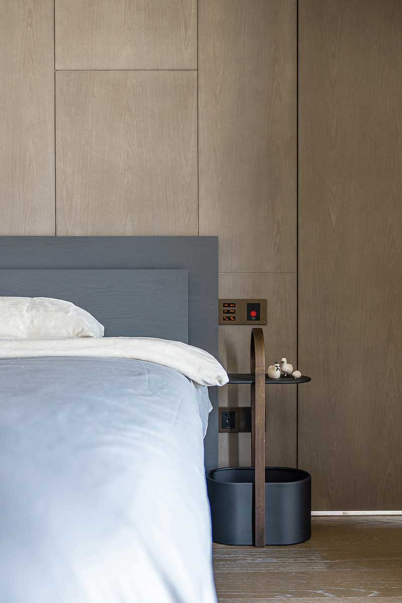 主臥家具以高級(jí)灰質(zhì)感為主，靜謐的色調(diào)也使空間充滿(mǎn)寧?kù)o的氣息。床頭背景墻改造成了整面水洗秋香木紋的護(hù)墻板+隱形門(mén)，令空間更加平衡，既有工業(yè)風(fēng)的粗獷感，造型又很簡(jiǎn)約，與現(xiàn)有裝修基礎(chǔ)完美融合。