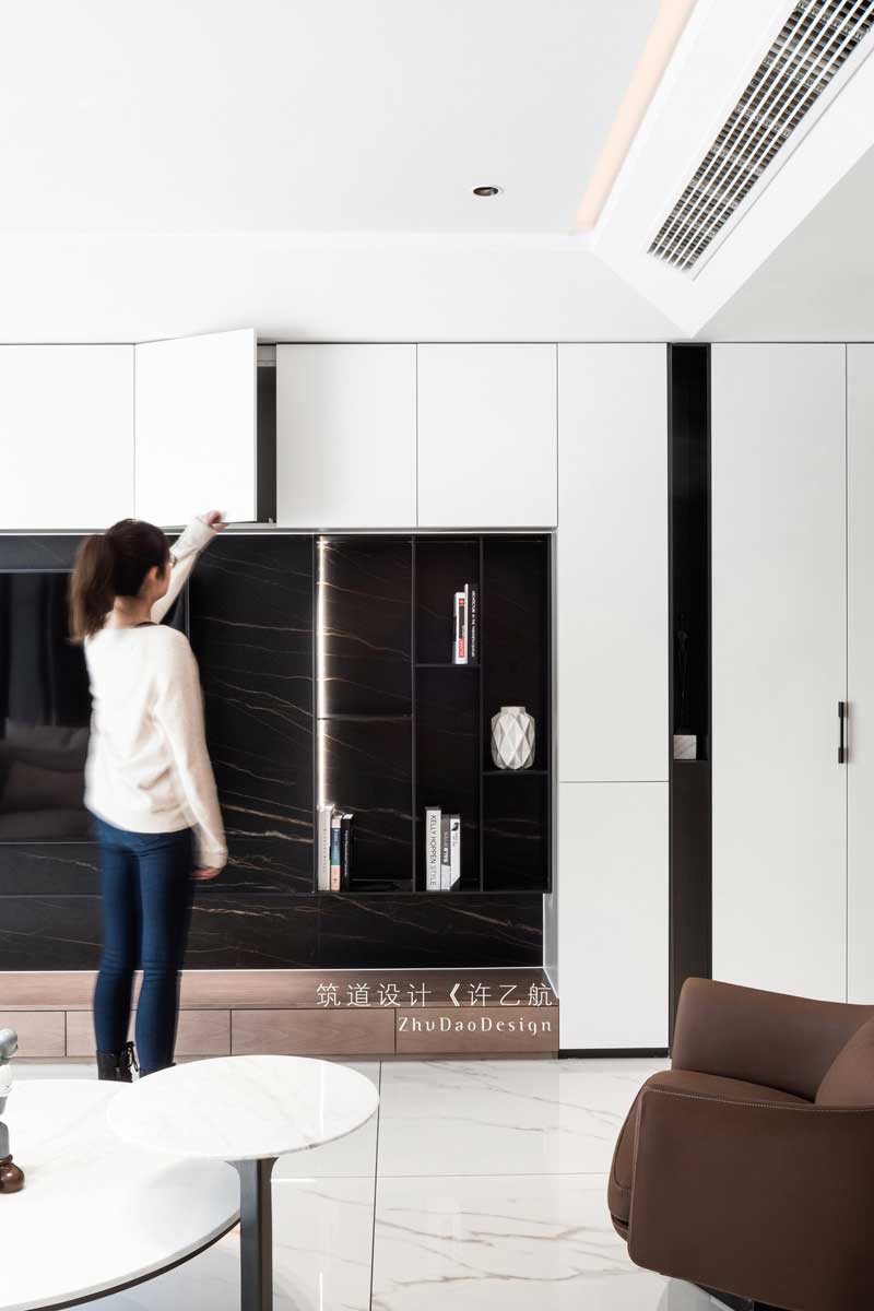  設(shè)計(jì)師拋棄傳統(tǒng)客廳的固有印象，將儲(chǔ)物柜與電視背景墻相結(jié)合，不僅增加了空間的儲(chǔ)物空間，在自然柔和的燈帶的襯托下，深灰色的啞光金屬條與深色大理石背景更有層次感，也成為了公共空間的一亮點(diǎn)所在。